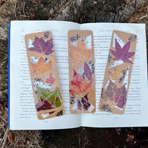 May include: Four brown bookmarks with pressed leaves in various shades of red, orange, and yellow. The bookmarks are made of cardboard and have a clear plastic coating over the leaves.