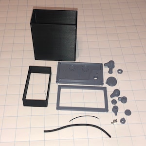 May include: A set of 3D printed parts for a project. The parts are in black and gray plastic. The parts include a box, a frame, a panel, and several small pieces.