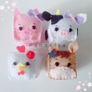 Puede incluir: Cuatro cubos de animales de fieltro hechos a mano: un cerdo rosa con un lazo, una vaca blanca y negra con un lazo, una gallina blanca con una cresta roja y un caballo marrón con una estrella. Los cubos tienen rasgos faciales lindos.