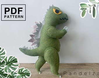 Puede incluir: Un juguete de peluche de dinosaurio de fieltro verde con una espalda de púas rosa y blanca. El juguete tiene un ojo amarillo y está de pie sobre una superficie de madera. El texto "PDF PATTERN" está en un cuadro negro en la esquina superior izquierda de la imagen.