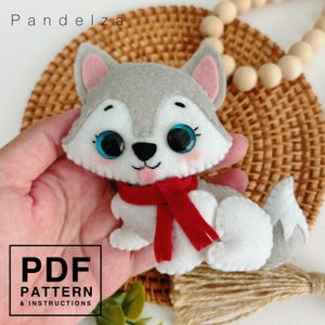 May include: A felt husky dog toy with a red scarf. The toy has big blue eyes and a white face. The toy is being held in a hand.