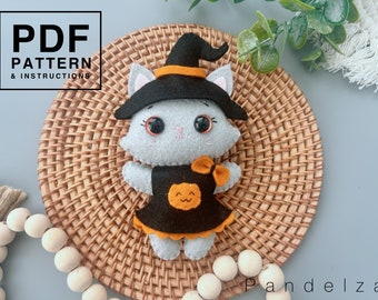 May include: A gray felt cat wearing a black witch hat with an orange band and a black dress with an orange pumpkin on the front. The cat is sitting on a woven brown wicker surface.