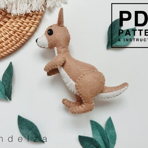 May include: A brown felt kangaroo toy with white stitching. The toy is sitting on a white surface with green felt leaves. The text "PDF PATTERN & INSTRUCTIONS" is in a black box in the top right corner of the image. The text "Pandeliza" is in the bottom left corner of the image.
