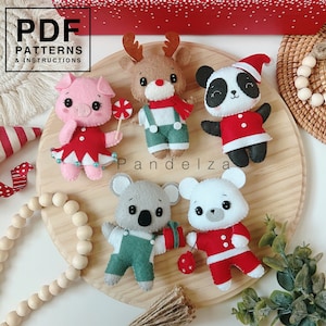 May include: A set of five felt Christmas ornaments, including a reindeer, panda, pig, koala, and polar bear. The ornaments are all wearing festive clothing and are arranged on a wooden surface. The text "Pandeliza" is visible in the image.