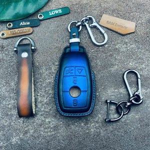 Peut inclure: Un couvre-clé bleu avec un porte-clés argenté. Le couvre-clé est bleu et argenté avec un trou de serrure et des boutons. Le porte-clés est attaché à une chaîne argentée.