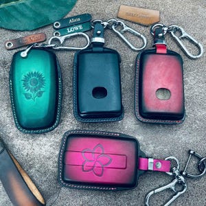 Puede incluir: Cuatro fundas de cuero para llaves con clips metálicos. Una funda verde con grabado de girasol, una negra, una con degradado rojo y negro, y una con degradado rosa y negro con grabado de flor. Incluye pequeñas etiquetas de cuero.