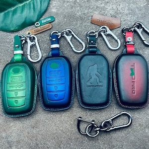 May include: Five different key fobs with leather covers. The key fobs are green, blue, black, and red. The key fobs have different designs and text on them, including "Big Goldy", "Karina", "Sasquatch", and "Trd Pro".