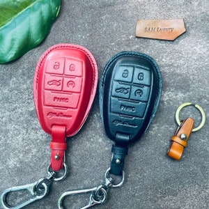 Può includere: Due copri chiavi in pelle per un portachiavi per auto. I copri chiavi sono rosso e nero e hanno un portachiavi argentato attaccato. I copri chiavi hanno pulsanti con la scritta "Panico" e "Alfa Romeo".