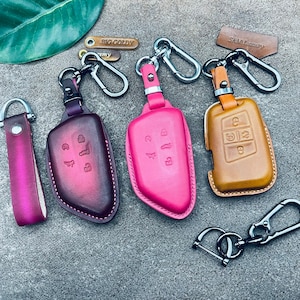 Könnte beinhalten: Vier Leder-Schlüsselhüllen in Pink, Braun und Burgunderrot mit silbernen Schlüsselringen. Die Schlüsselhüllen haben geprägte Designs und die Schlüsselringe haben einen silbernen Clip.