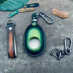 May include: A collection of leather keychains and key holders in various colors. Includes a green key holder, a brown and orange keychain, and several small tags with names like "Alicia" and "Karina".