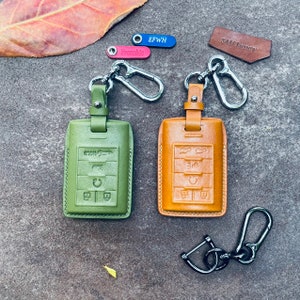 May include: Two leather key fobs with metal key rings and a silver key chain. The key fobs are green and brown and have embossed buttons. The text "SAM Luxury" is on a brown leather tag.