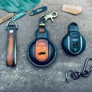 Peut inclure: Trois porte-clés en cuir avec du cuir de différentes couleurs et des noms personnalisés. Les porte-clés sont attachés à des porte-clés de voiture. Les noms sur les porte-clés sont "Big Goldy", "Karina", "Alicia" et "Sam Luxury".