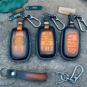 May include: Three brown and black gradient leather key fob covers with metal clips. One cover features a skull design, while two show button icons. Includes small leather tags with names like Alicia, Van Vleet, Lowe, and Sam Lammari.