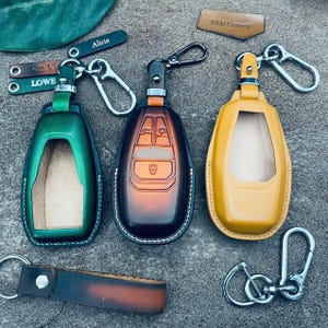 Peut inclure: Trois étuis de porte-clés en cuir vert, marron et jaune, chacun avec un mousqueton argenté. L'étui marron comporte des boutons en relief. Des étiquettes en cuir supplémentaires avec des noms sont également présentes.