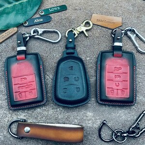 May include: Three leather key fobs with different colored stitching. The key fobs are red, black, and red with a black trim. Each key fob has a different name on it: "Lowe", "Alicia", and "Sam Luxury".