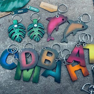 Chaveiros iniciais de golfinho Monstera Chaveiros personalizados Chaveiros com letras brilhantes Chaveiros personalizados com alfabeto Bolsa de presente para bagagem Carteira com pingente de etiqueta