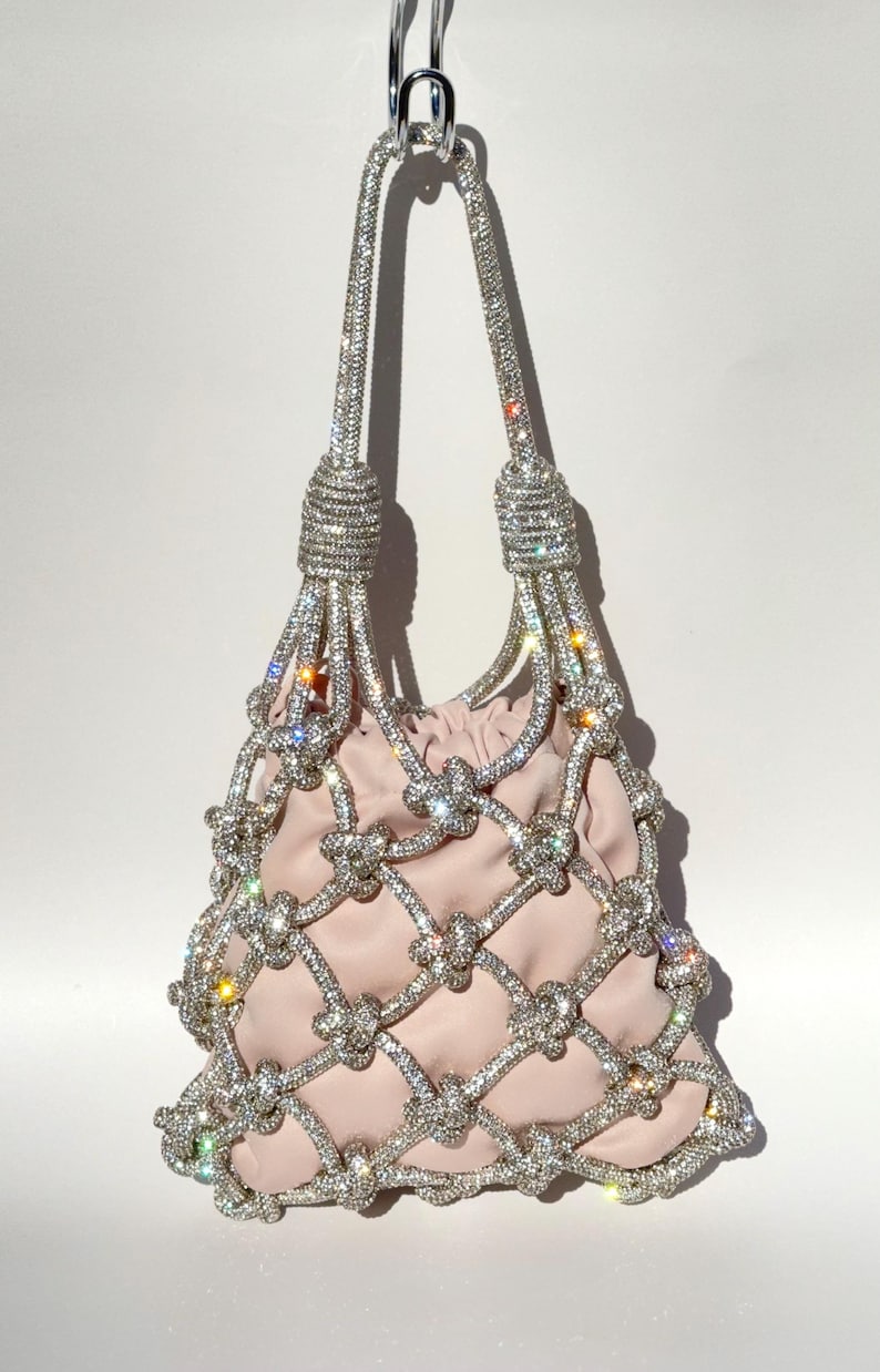 May include: A pink handbag with a knotted design and a silver chain strap. The bag is covered in rhinestones.