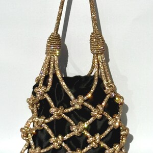 May include: A black velvet bag with a gold chain-like design. The bag has a knotted design and is adorned with rhinestones.