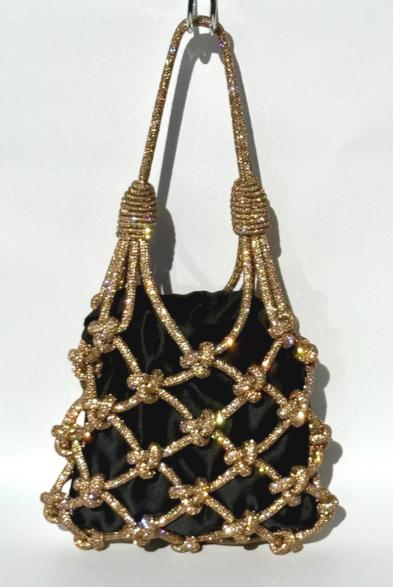 May include: A black velvet bag with a gold chain-like design. The bag has a knotted design and is adorned with rhinestones.