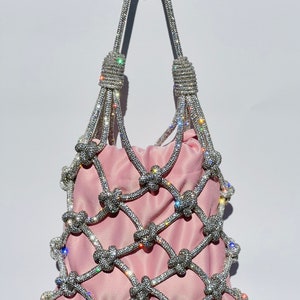 May include: A pink satin bag with a crystal-encrusted net design. The bag has a top handle and is decorated with sparkling rhinestones.