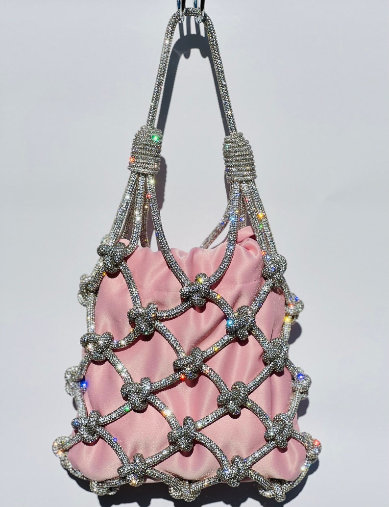 May include: A pink satin bag with a crystal-encrusted net design. The bag has a top handle and is decorated with sparkling rhinestones.