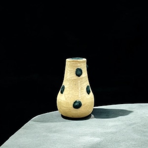 Könnte beinhalten: Eine kleine, cremefarbene Keramikvase mit craquelé-Glasur und dunkelgrünen Punkten.