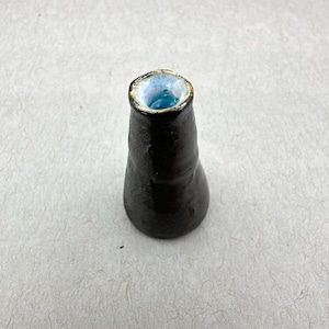 Op de afbeelding: Een kleine zwarte keramische vaas met een blauw en wit geglazuurd interieur. De vaas heeft een ronde basis en een smalle opening.