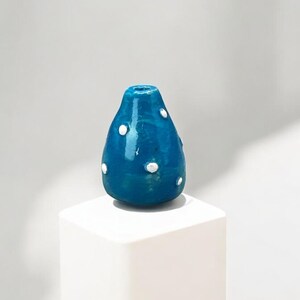 Op de afbeelding: Een kleine, tealblauwe keramische vaas met witte stippen. De vaas staat op een wit voetstuk.
