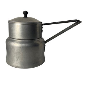 May include: A vintage aluminum stovetop coffee maker with a lid and a long handle. The coffee pot is silver with a black knob on the lid. The handle is attached to the side of the pot. The coffee maker is designed to sit on a stovetop.