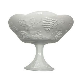 May include: White milk glass pedestal bowl with a grapevine design. The bowl has a scalloped edge and a pedestal base.