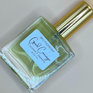 May include: A clear glass bottle with a gold cap filled with a light green liquid. The bottle has a white label with the text "Good Courage" and "Coconut | Jasmine body oil" printed on it.