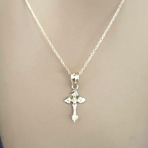 May include: A silver necklace with a detailed cross pendant. The cross features a figure of Jesus Christ. The chain is fine and hangs against a neutral backdrop, showcasing the pendant's intricate design.