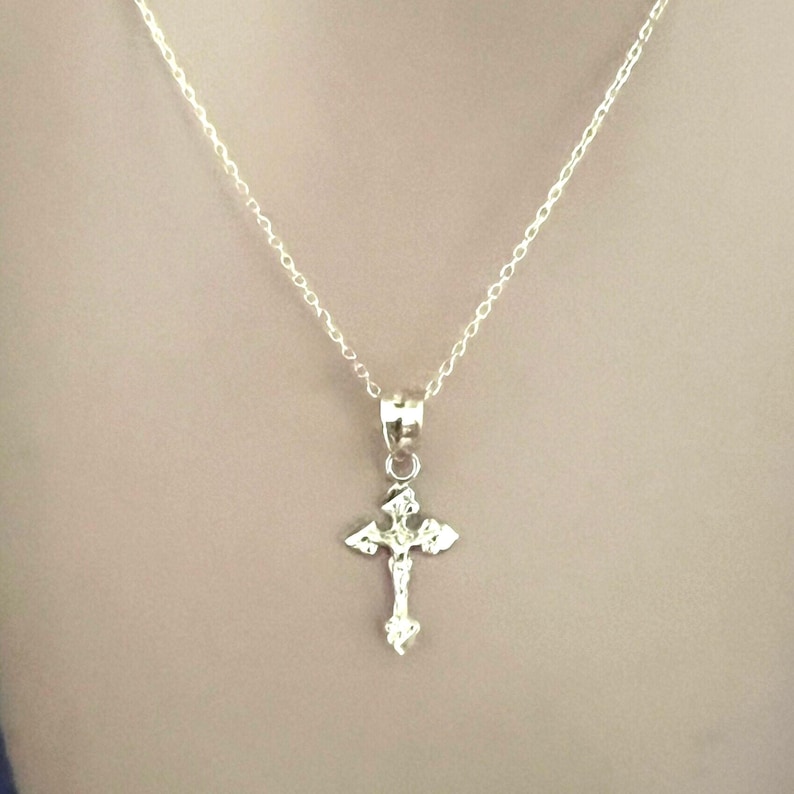 May include: A silver necklace with a detailed cross pendant. The cross features a figure of Jesus Christ. The chain is fine and hangs against a neutral backdrop, showcasing the pendant's intricate design.