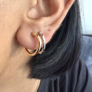 Op de afbeelding: Close-up van twee oorringen. E&eacute;n is goudkleurig en de andere zilverkleurig. De oorbellen worden op het oor gedragen. De gouden oorring zit voor de zilveren oorring. De oorbellen hebben een eenvoudig, klassiek ontwerp.