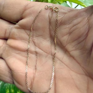 May include: A delicate gold chain bracelet featuring a classic mariner link design. The bracelet is constructed with small, uniform oval links and is secured with a circular spring ring clasp at the top, showcasing a polished metallic finish.