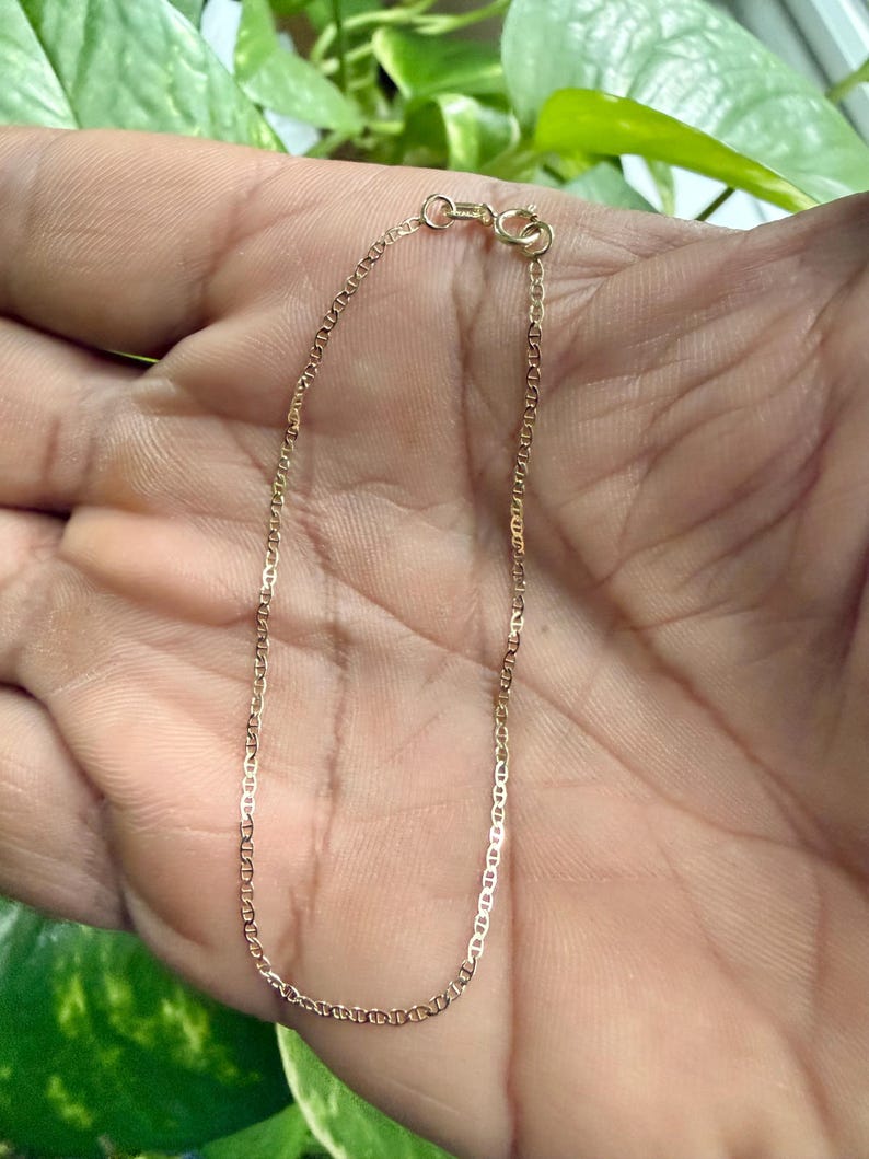 May include: A delicate gold chain bracelet featuring a classic mariner link design. The bracelet is constructed with small, uniform oval links and is secured with a circular spring ring clasp at the top, showcasing a polished metallic finish.