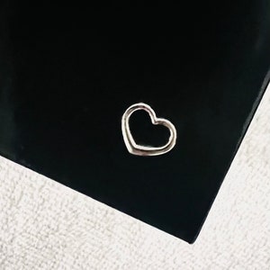 May include: A silver heart-shaped charm on a black background.