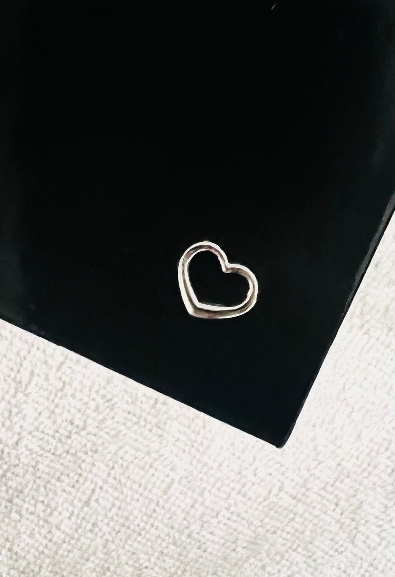 May include: A silver heart-shaped charm on a black background.