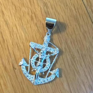 K&ouml;nnte beinhalten: Silberfarbener Anh&auml;nger mit Anker-Design, Kreuz und Figur, verziert mit funkelnden Akzenten. Das Design des Anh&auml;ngers erzeugt einen auff&auml;lligen Kontrast. Ein Schmuckst&uuml;ck mit religi&ouml;sem Thema.