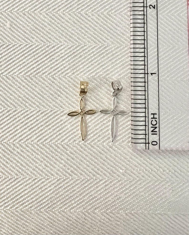Puede incluir: Dos peque&ntilde;os colgantes de cruz, uno dorado y otro plateado, se muestran junto a una regla en pulgadas. Las cruces tienen un dise&ntilde;o abierto y delicado. La regla muestra medidas en pulgadas.