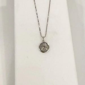 Peut inclure: Un collier argent&eacute; avec un petit pendentif rond. Le pendentif pr&eacute;sente un relief d&eacute;taill&eacute; d'un ange. La cha&icirc;ne est fine et le pendentif est centr&eacute;, cr&eacute;ant un design simple et &eacute;l&eacute;gant.
