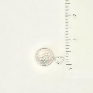 May include: A silver heart charm pendant, approximately the size of a US dime, shown next to a ruler.