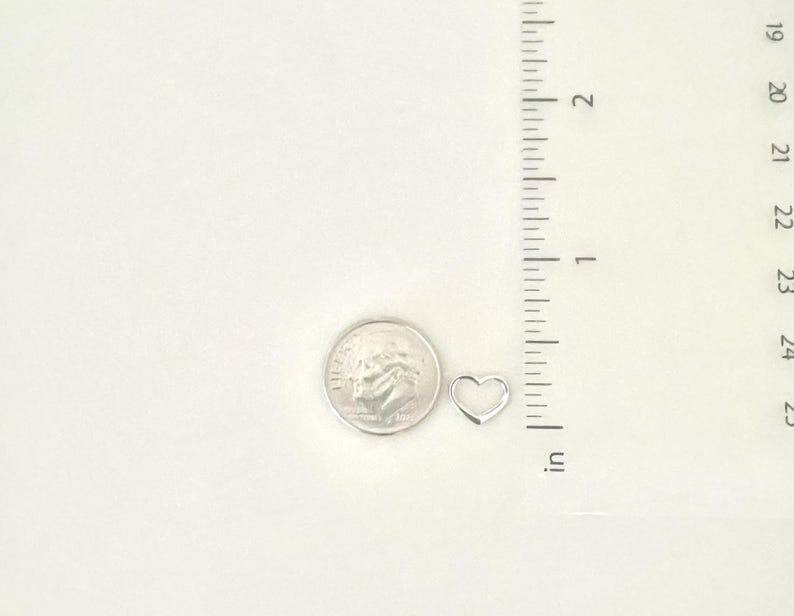 May include: A silver heart charm pendant, approximately the size of a US dime, shown next to a ruler.