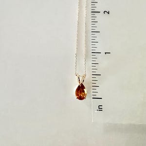 May include: A gold-colored necklace with a teardrop-shaped, amber-colored gemstone pendant. The pendant is approximately 0.5 inches in length. The necklace is displayed against a white background.