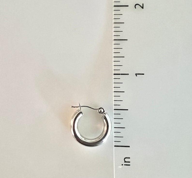K&ouml;nnte beinhalten: Ein einzelner, gl&auml;nzender silberner Creolen-Ohrring. Der Ohrring hat einen Durchmesser von ca. 1,9 cm. Der Ohrring wird vor einem wei&szlig;en Hintergrund mit einem Zollstock zur Gr&ouml;&szlig;enbestimmung gezeigt.