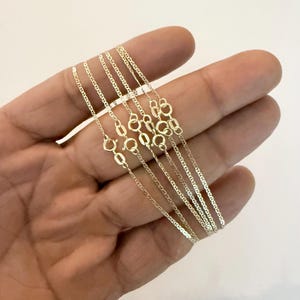 May include: A collection of multiple thin gold chains, each featuring a delicate mariner link design and a small, circular spring ring clasp. The chains are crafted from a polished yellow gold metal, showcasing a consistent, uniform link pattern.