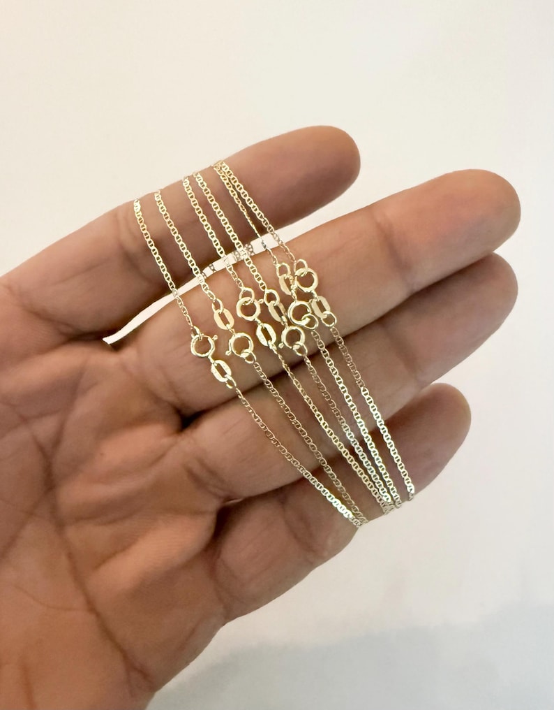 May include: A collection of multiple thin gold chains, each featuring a delicate mariner link design and a small, circular spring ring clasp. The chains are crafted from a polished yellow gold metal, showcasing a consistent, uniform link pattern.