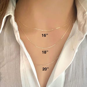 May include: Three gold chain necklaces in different lengths: 16 inches, 18 inches, and 20 inches. The necklaces are shown on a model wearing a white shirt.