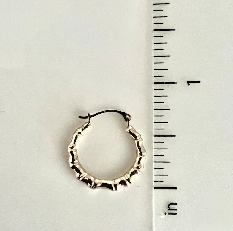 Puede incluir: Pendiente de aro plateado con dise&ntilde;o de bamb&uacute;. El pendiente mide aproximadamente 2,5 cm de di&aacute;metro. Se muestra sobre un fondo blanco junto a una regla.