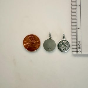 Peut inclure: Deux petits pendentifs en argent, dont un avec un ange, &agrave; c&ocirc;t&eacute; d'un penny et d'une r&egrave;gle. Le pendentif ange a un relief d&eacute;taill&eacute; d'un ch&eacute;rubin. L'autre pendentif est uni. La r&egrave;gle montre des mesures en centim&egrave;tres.